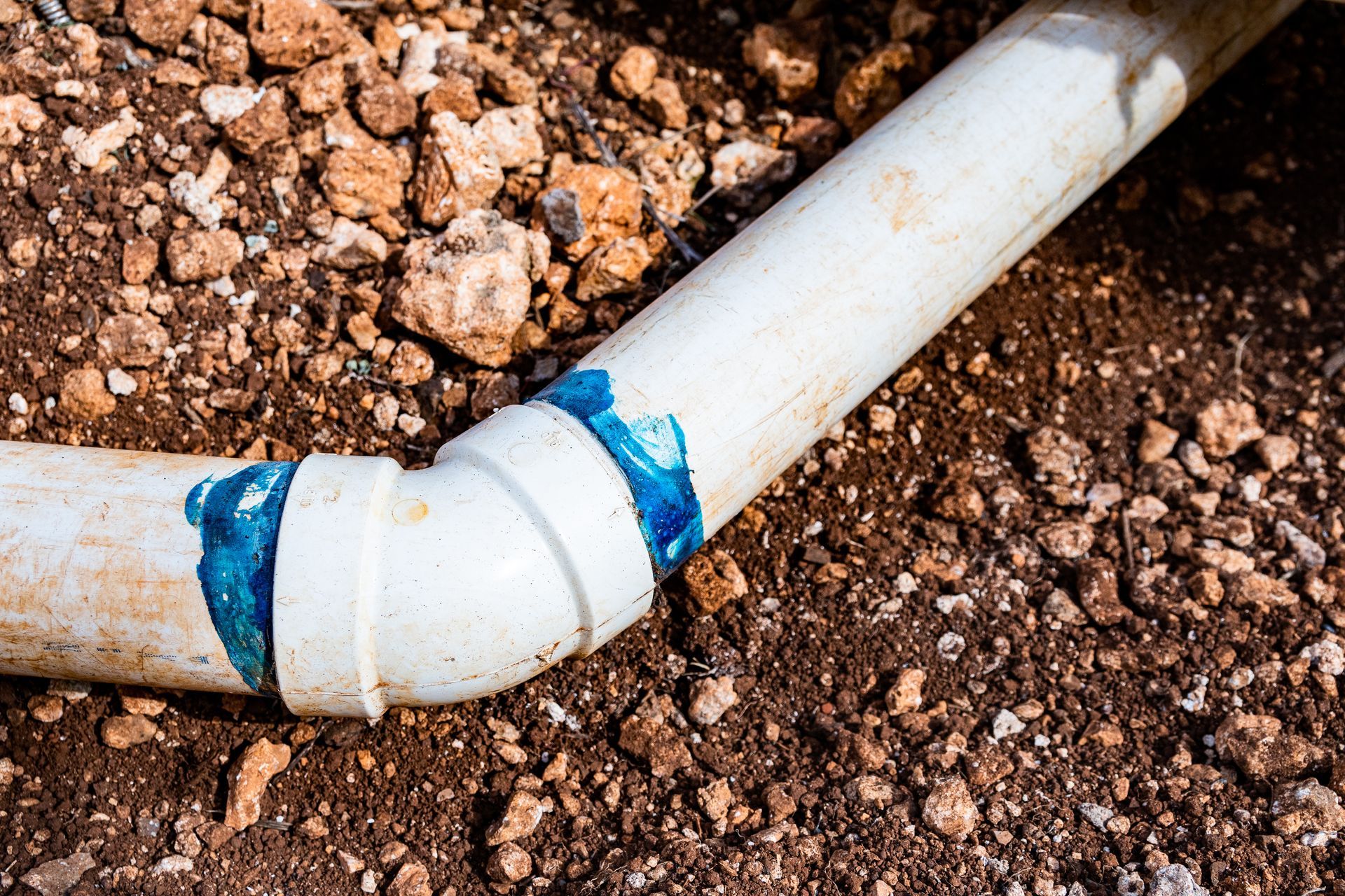 White PVC pipe elbow joint with blue tape leaking in brown soil
