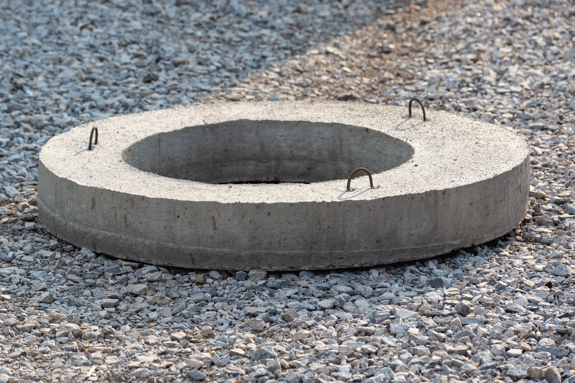 Concrete manhole ring with metal loops on gravel ground
