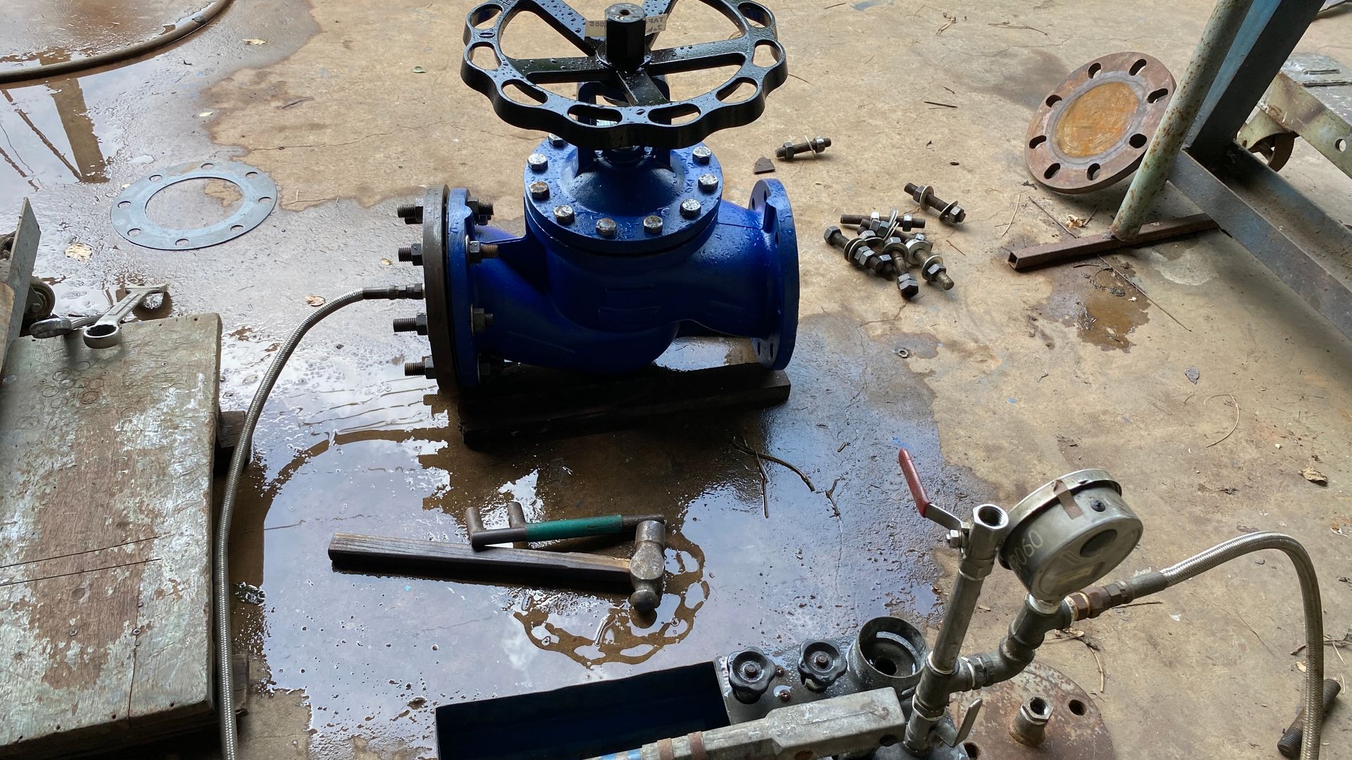 Blue industrial valve assembly on a wet workshop floor, with tools and scattered parts nearby.
