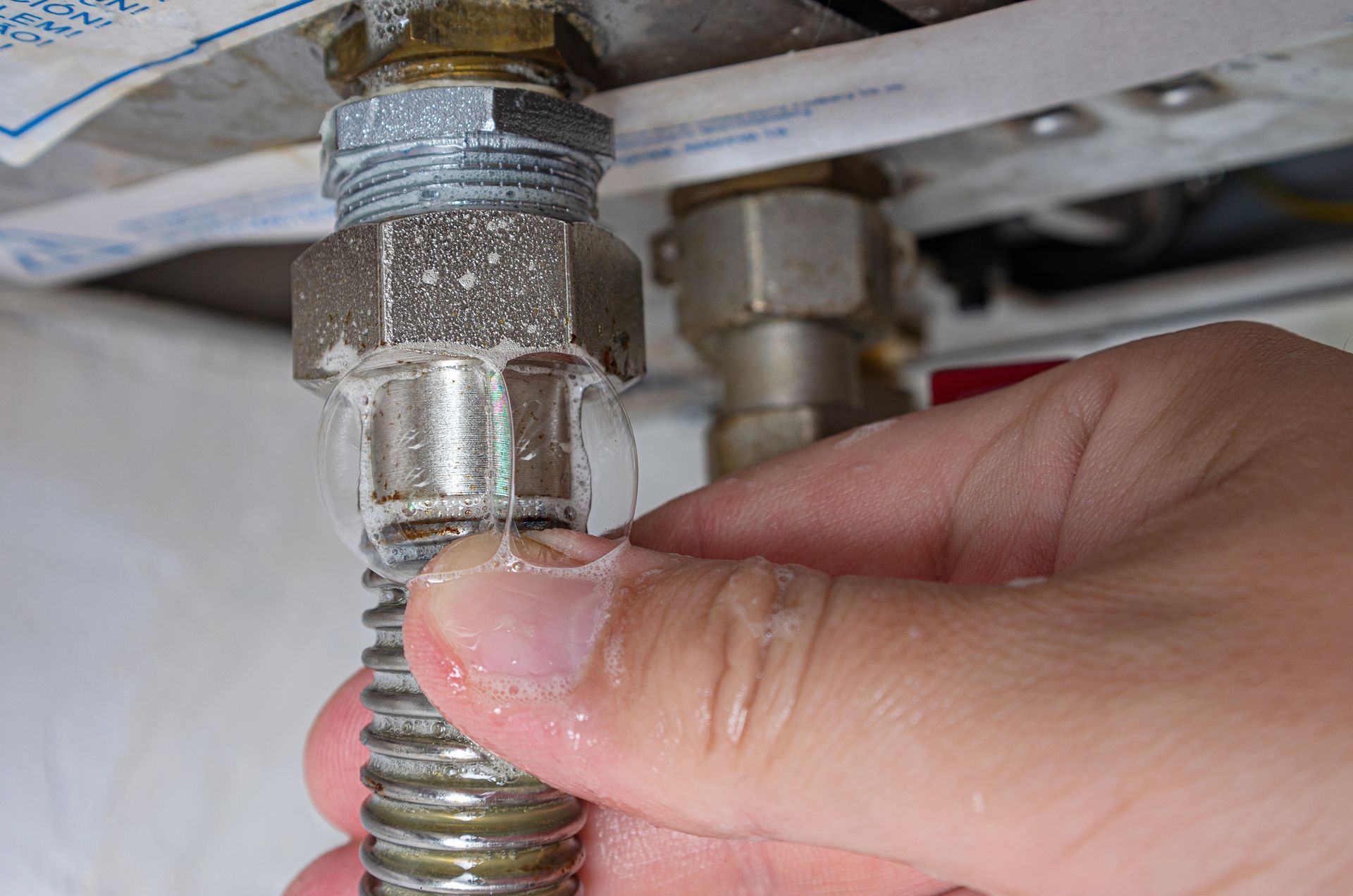 Hand tightening a threaded hose connection under a sink with a wrench nearby