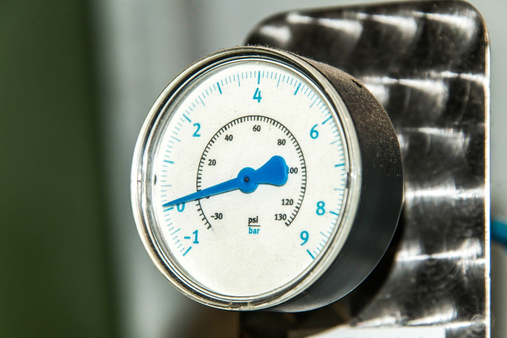 Close-up of a blue analog dial gauge on a metal wall plate.