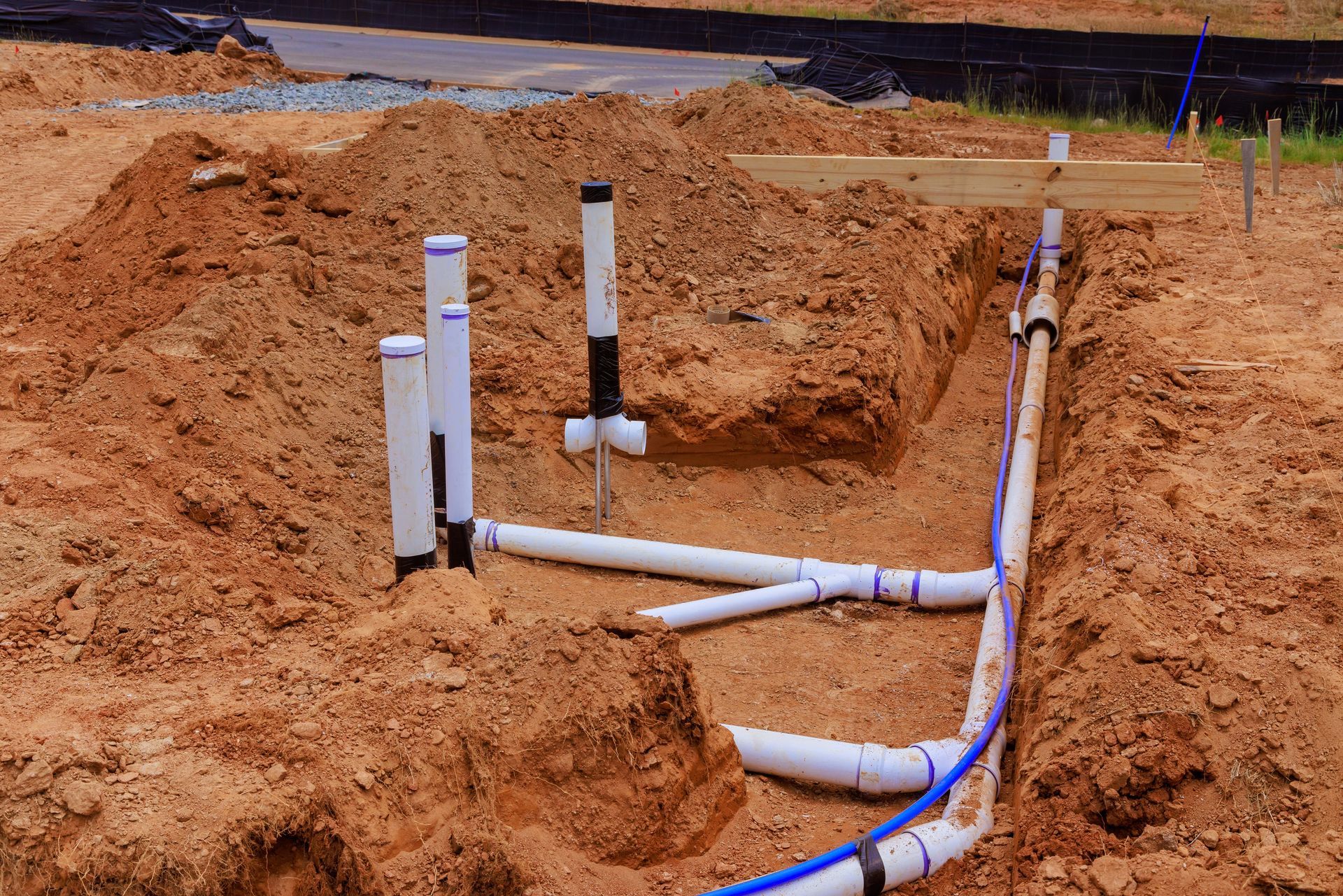 White PVC pipes installed in a dirt trench at a construction site