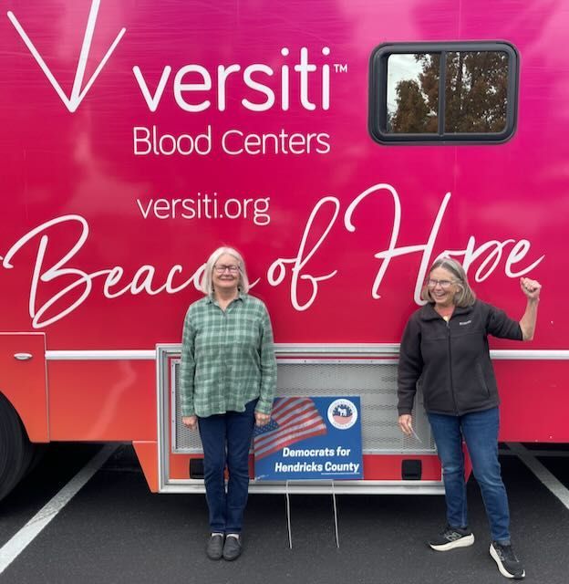 Versiti Blood Centers mobile unit. One holds up a fist. A sign for Democrats is present.