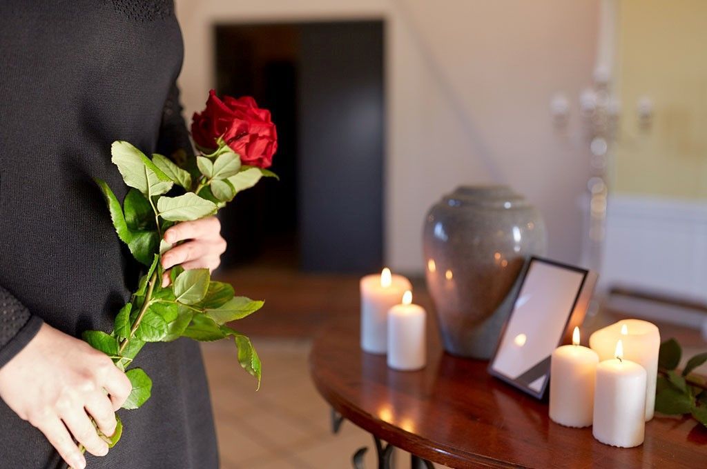 Una persona tiene in mano delle rose rosse accanto a candele accese e una foto incorniciata su un tavolo.