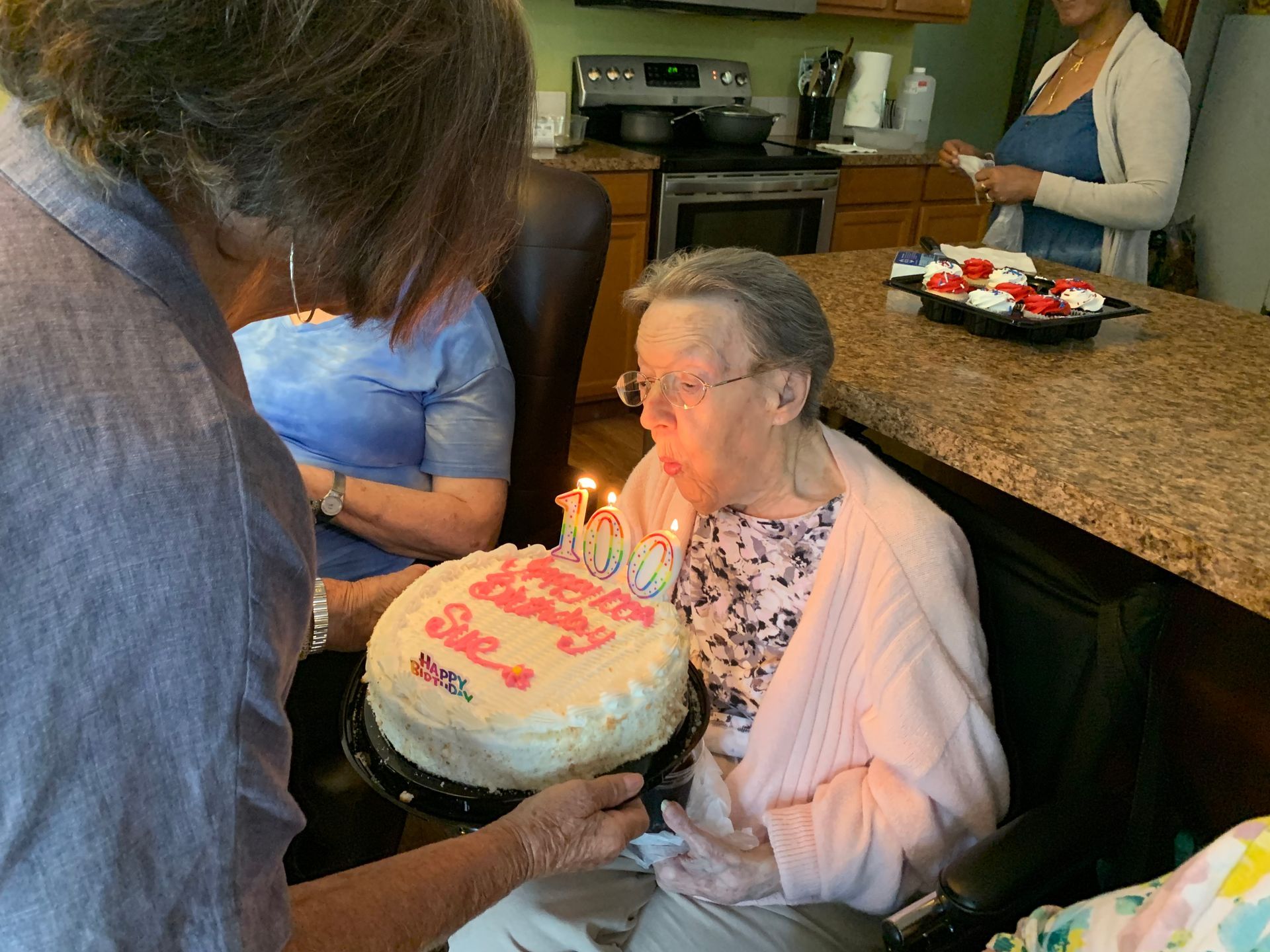 Woman in a pink cardigan blowing out candles on a birthday cake