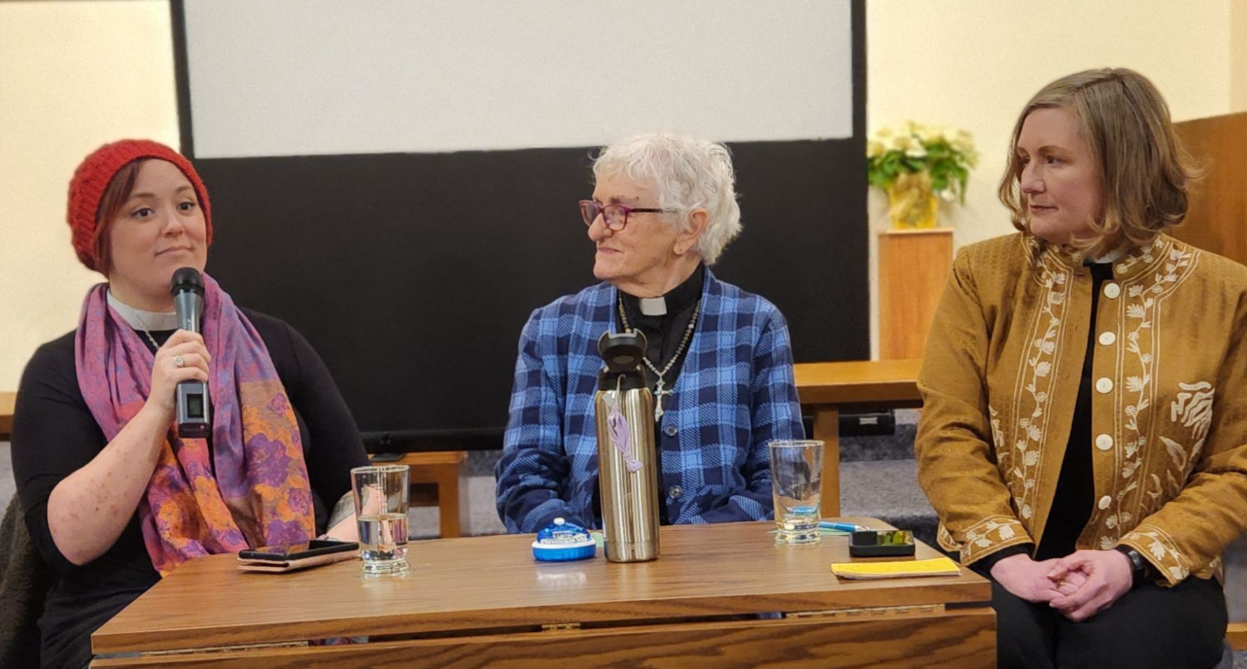 Three panelists seated at a table during a discussion, one speaking into a microphone.