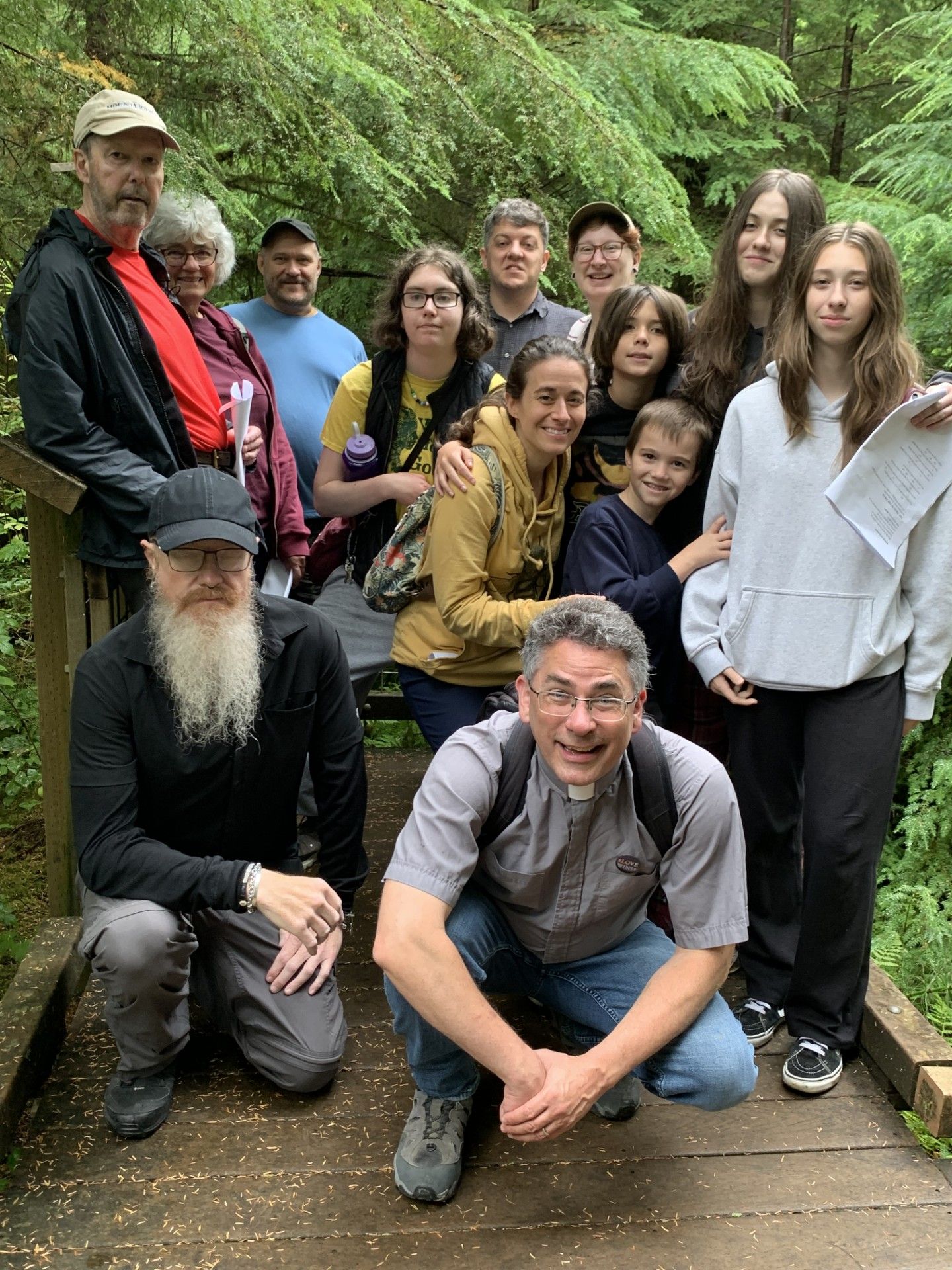 Group of smiling people posing on a wooden trail in a lush green forest