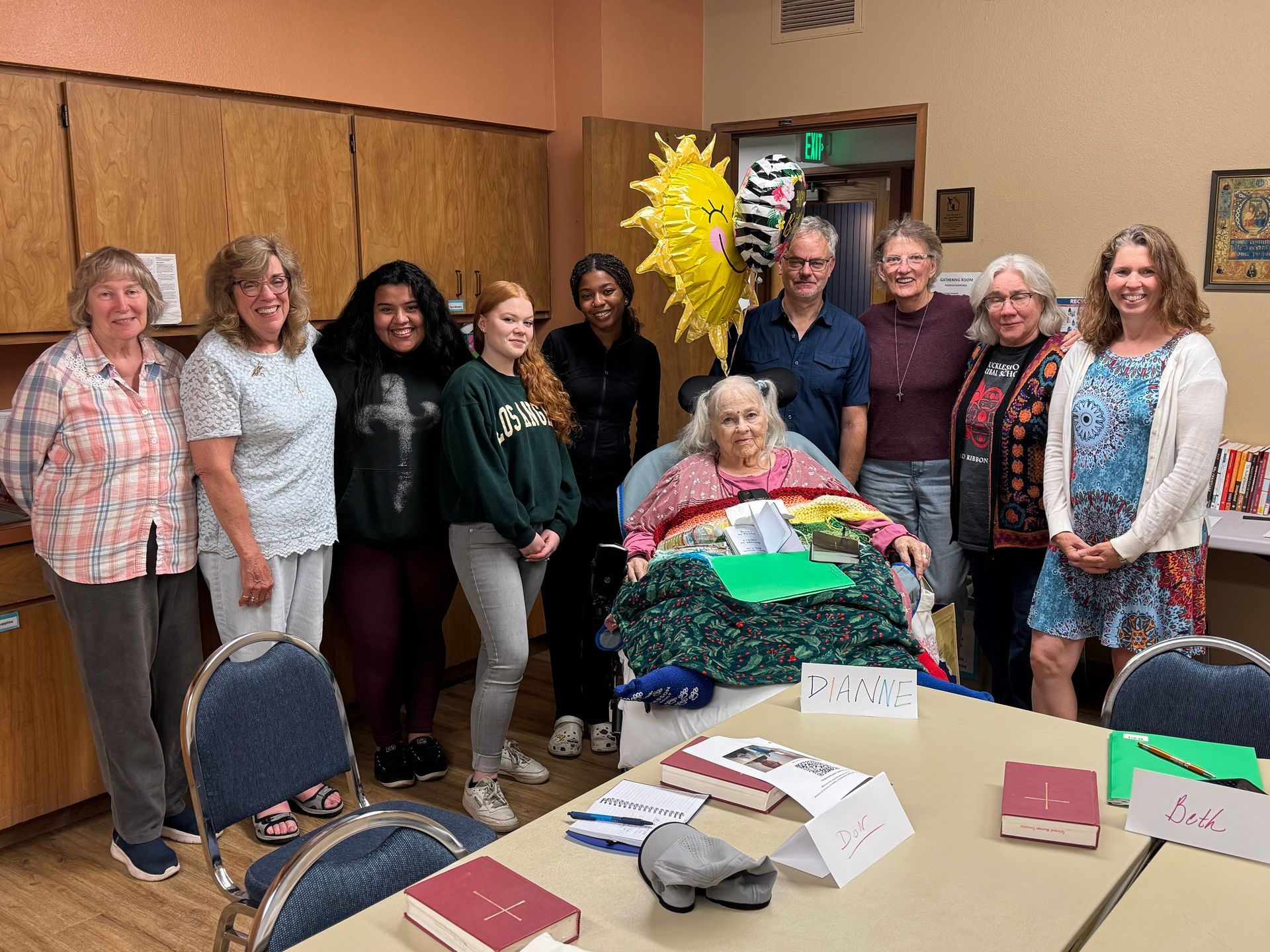 Group of people standing in a room around a table with craft supplies and a bright sun decoration on the wall