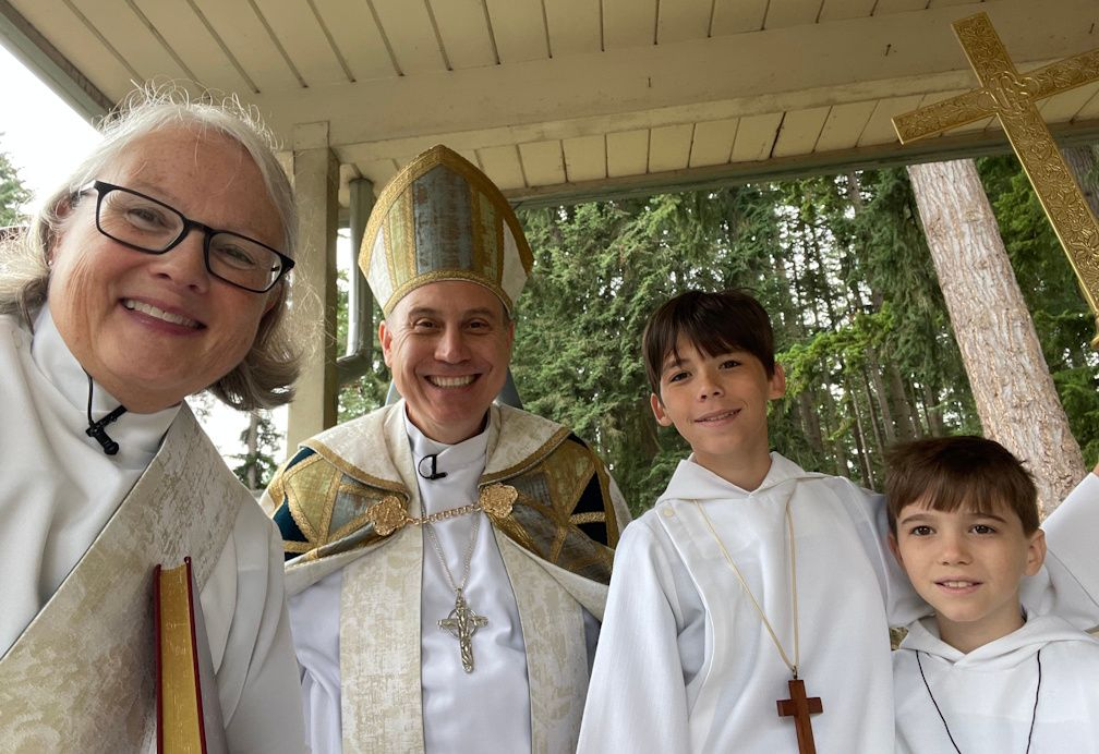 Four people in white ceremonial robes smiling outdoors under a porch