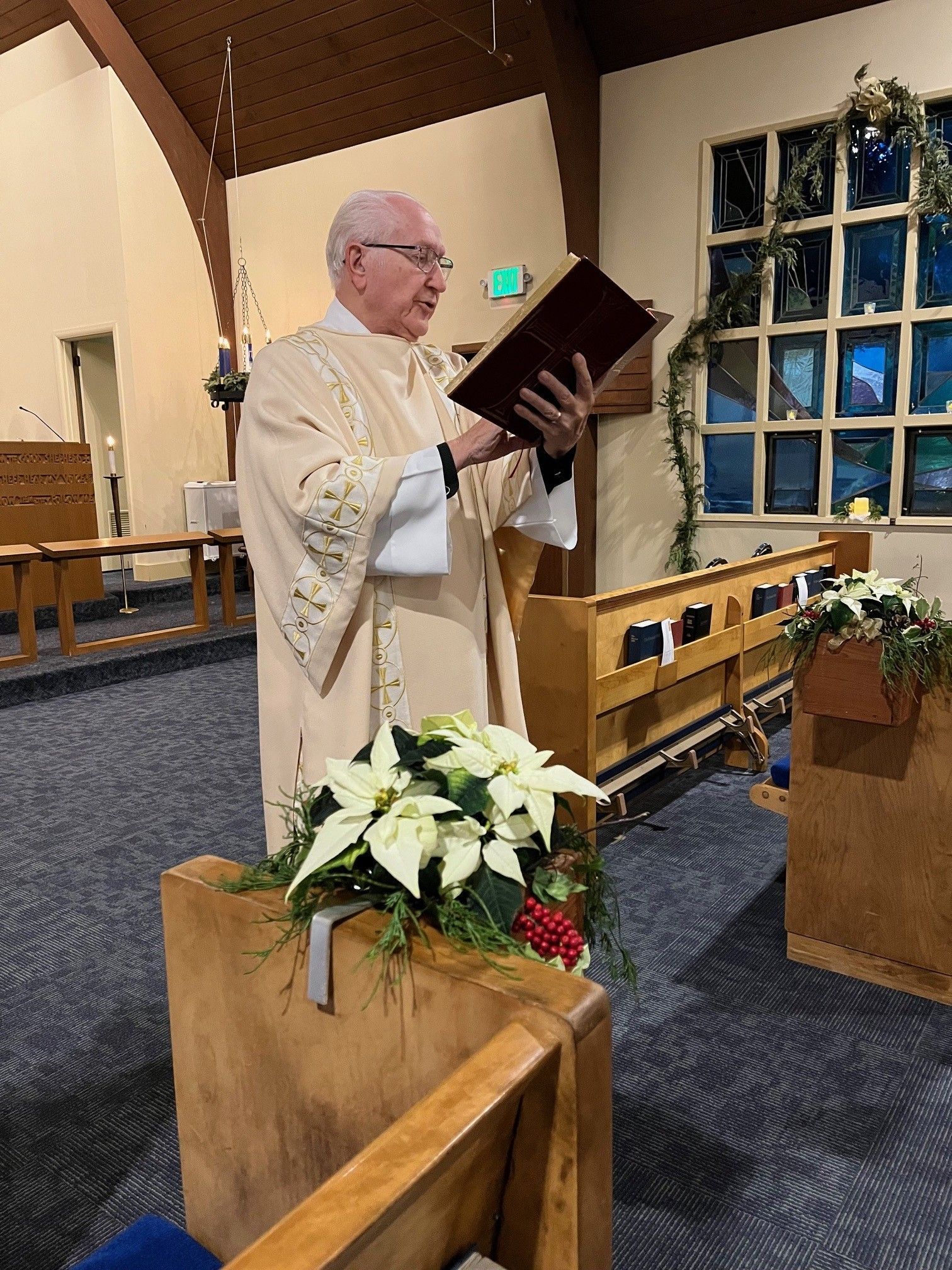 Priest in white vestments reading from a book at the altar inside a church.