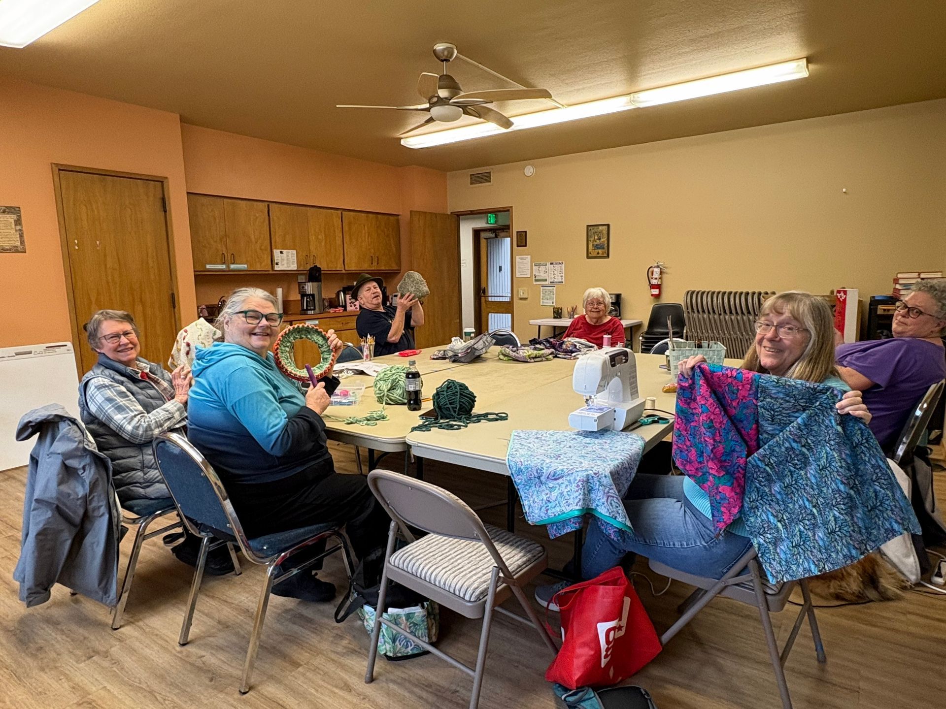 People seated around a large table in a community room, chatting during a gathering.