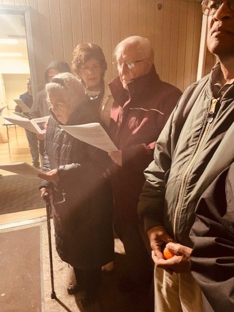 People reading from papers in a warmly lit indoor hallway, standing close together near a doorway
