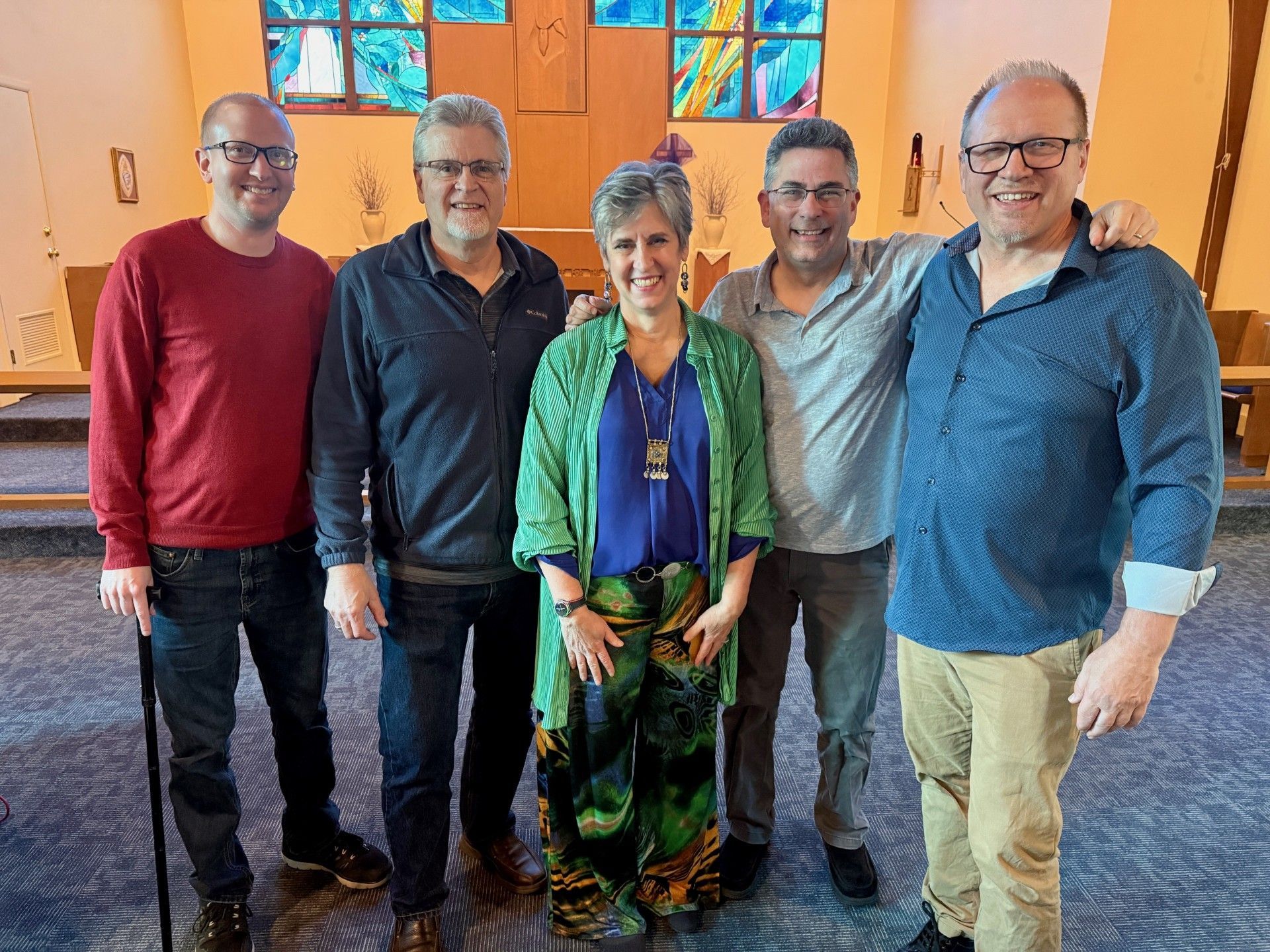 Five people standing together indoors in a carpeted room, smiling at the camera.
