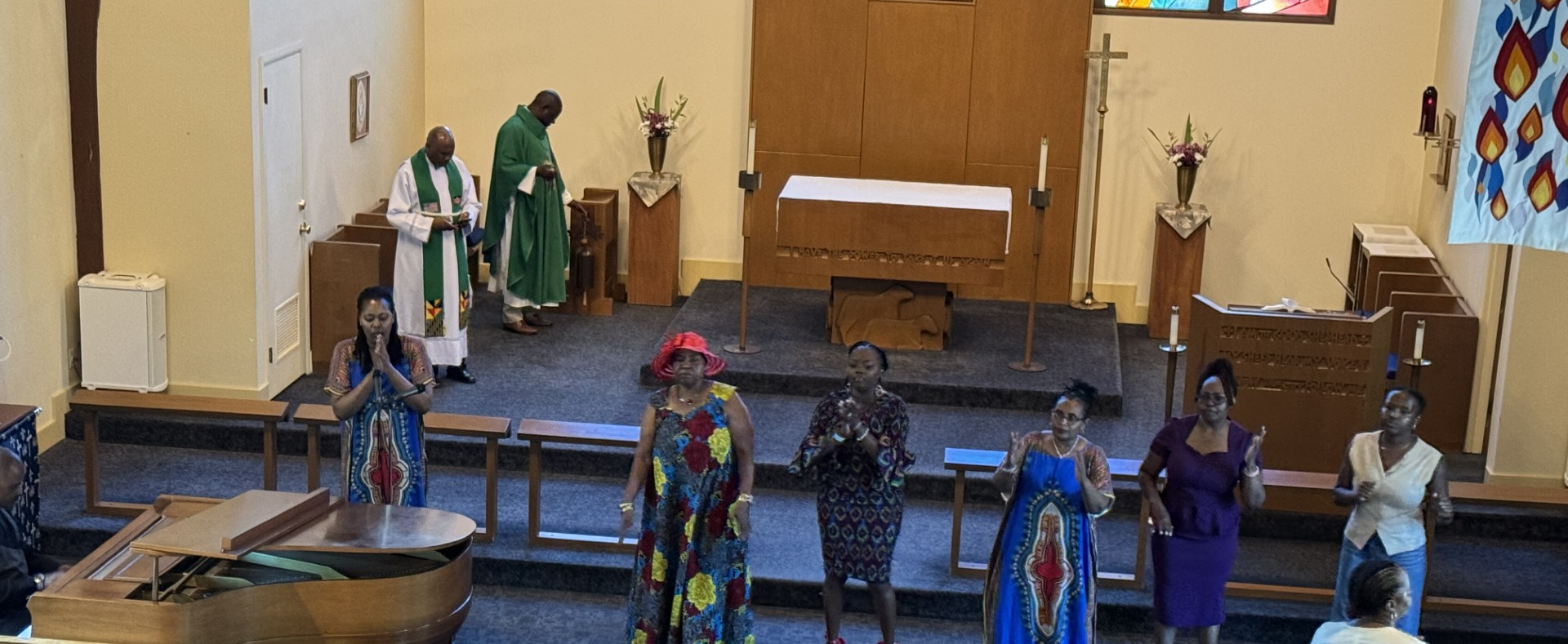 People standing on a church stage beside a baptismal pool, with clergy in green robes in the background