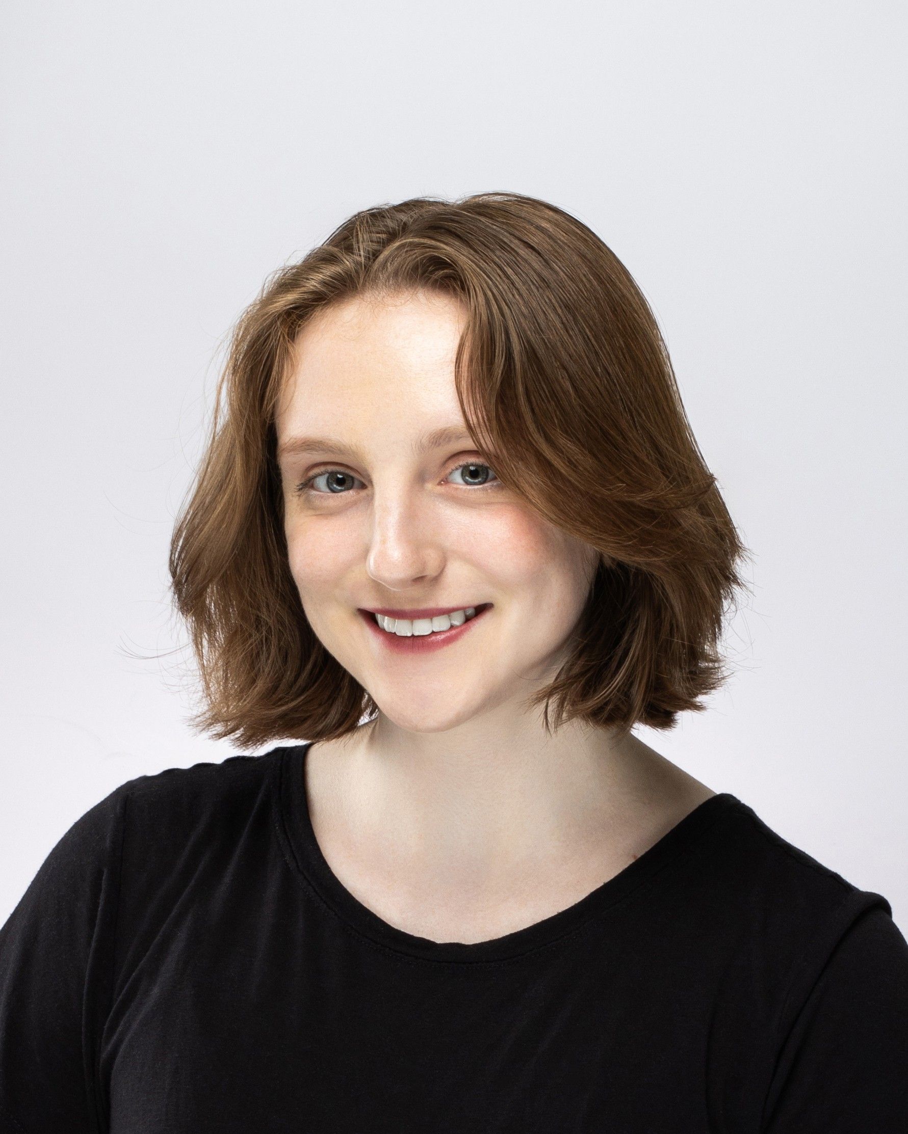 Portrait of a smiling person with short brown hair wearing a black shirt against a light gray background