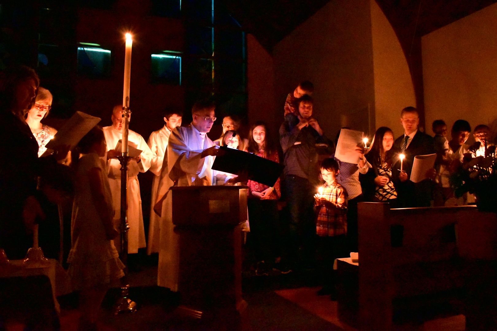 People holding candles in a dimly lit indoor vigil or ceremony