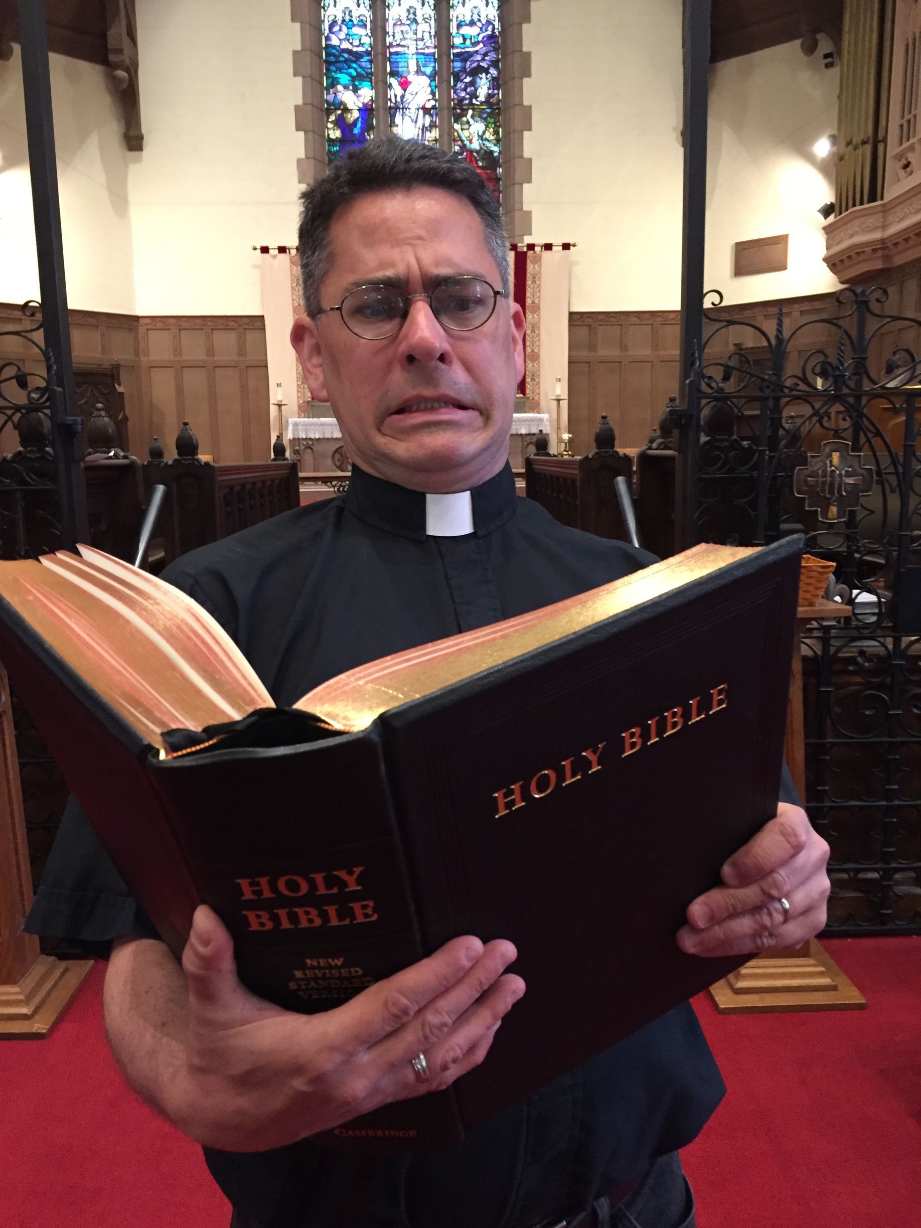Priest in black shirt holding an open Holy Bible inside a church