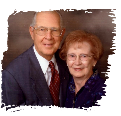 Portrait of an older couple in formal attire, smiling against a brown studio backdrop
