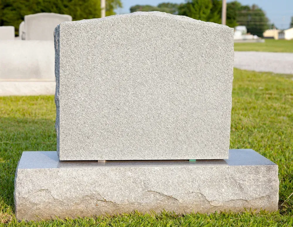 Blank gray gravestone on a base in a cemetery grass setting