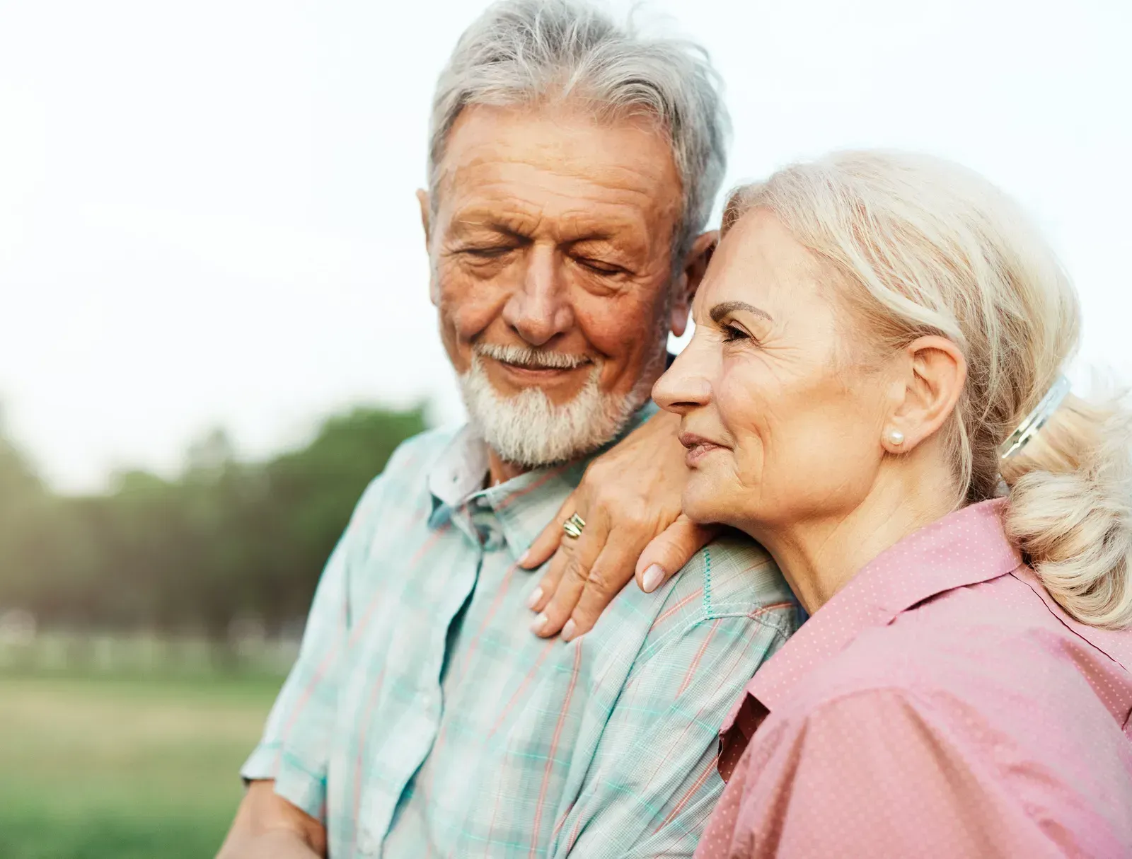 Smiling older couple embracing outdoors, with trees blurred in the background