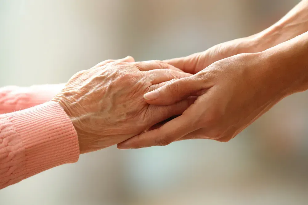 Two hands gently holding, one elderly hand and one younger hand, symbolizing care and support
