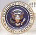 Seal of the President of the United States: gold, blue, and white eagle with stars and text.
