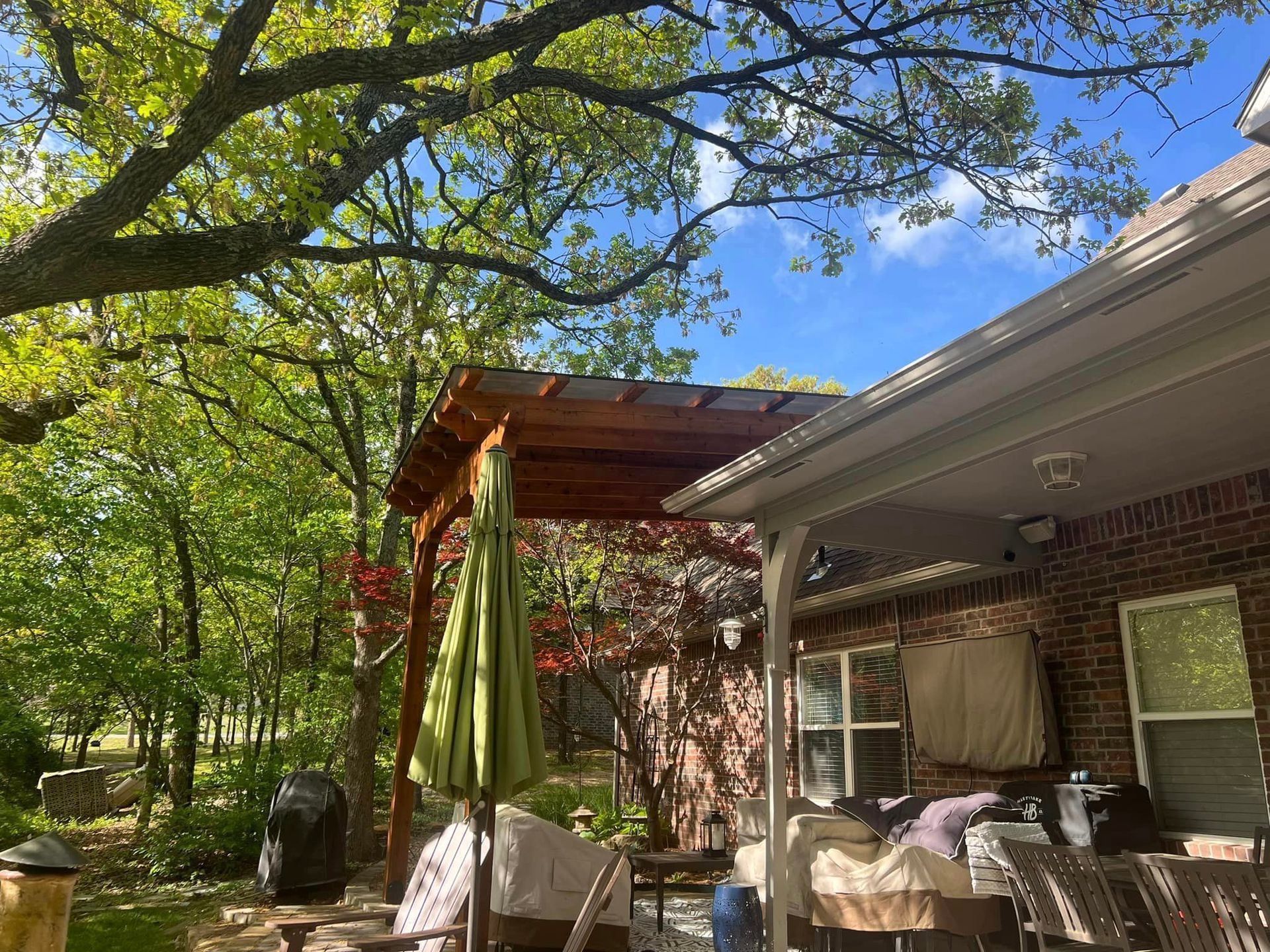 A patio with a pergola and umbrella on a sunny day.