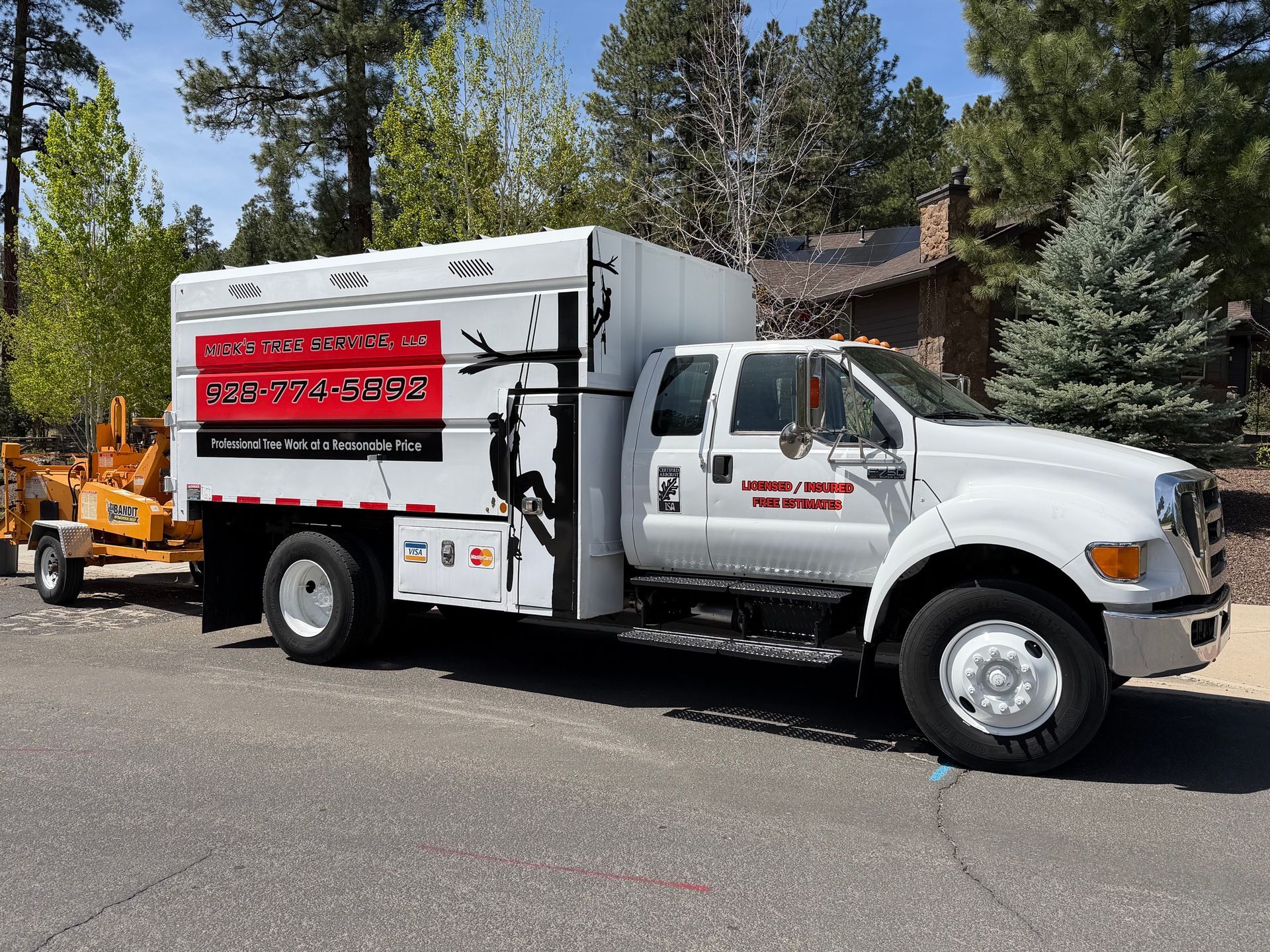 Utility trucks and a bucket lift working on a tree-lined residential street, with cones and a worker visible.