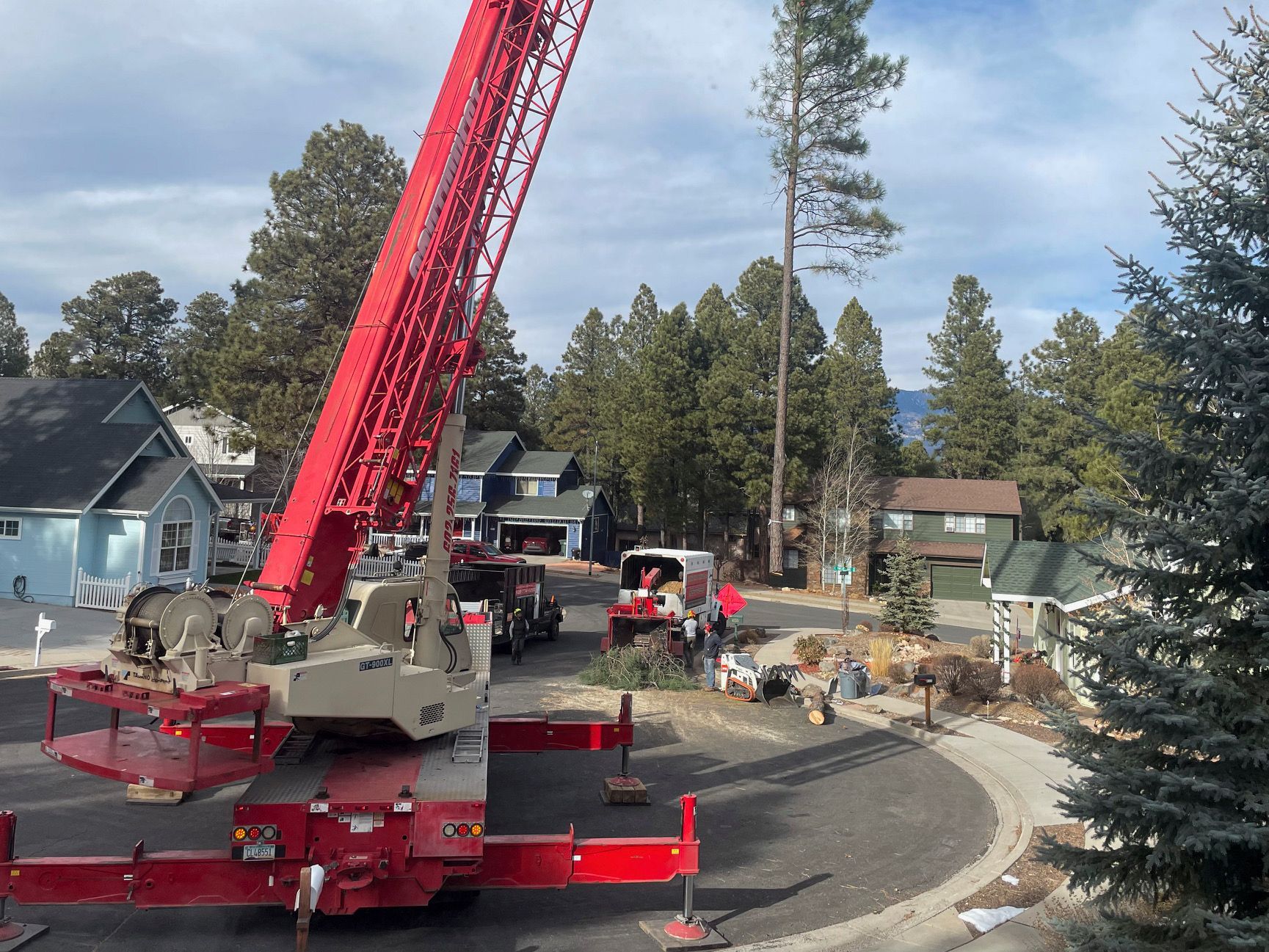 Red crane at a residential construction site with workers and trees in the background