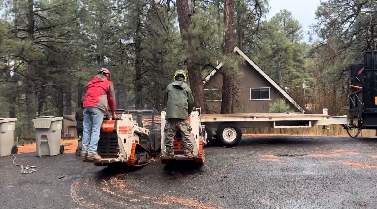 Two workers operating a cherry picker beside a cabin in a wooded area