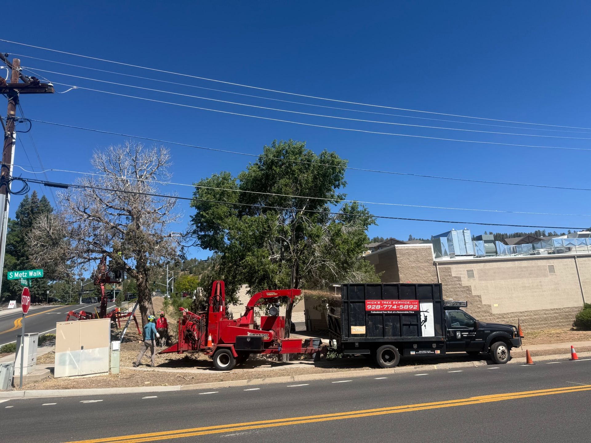 Red tow truck and black utility truck parked by a roadside under a clear blue sky, with workers nearby.