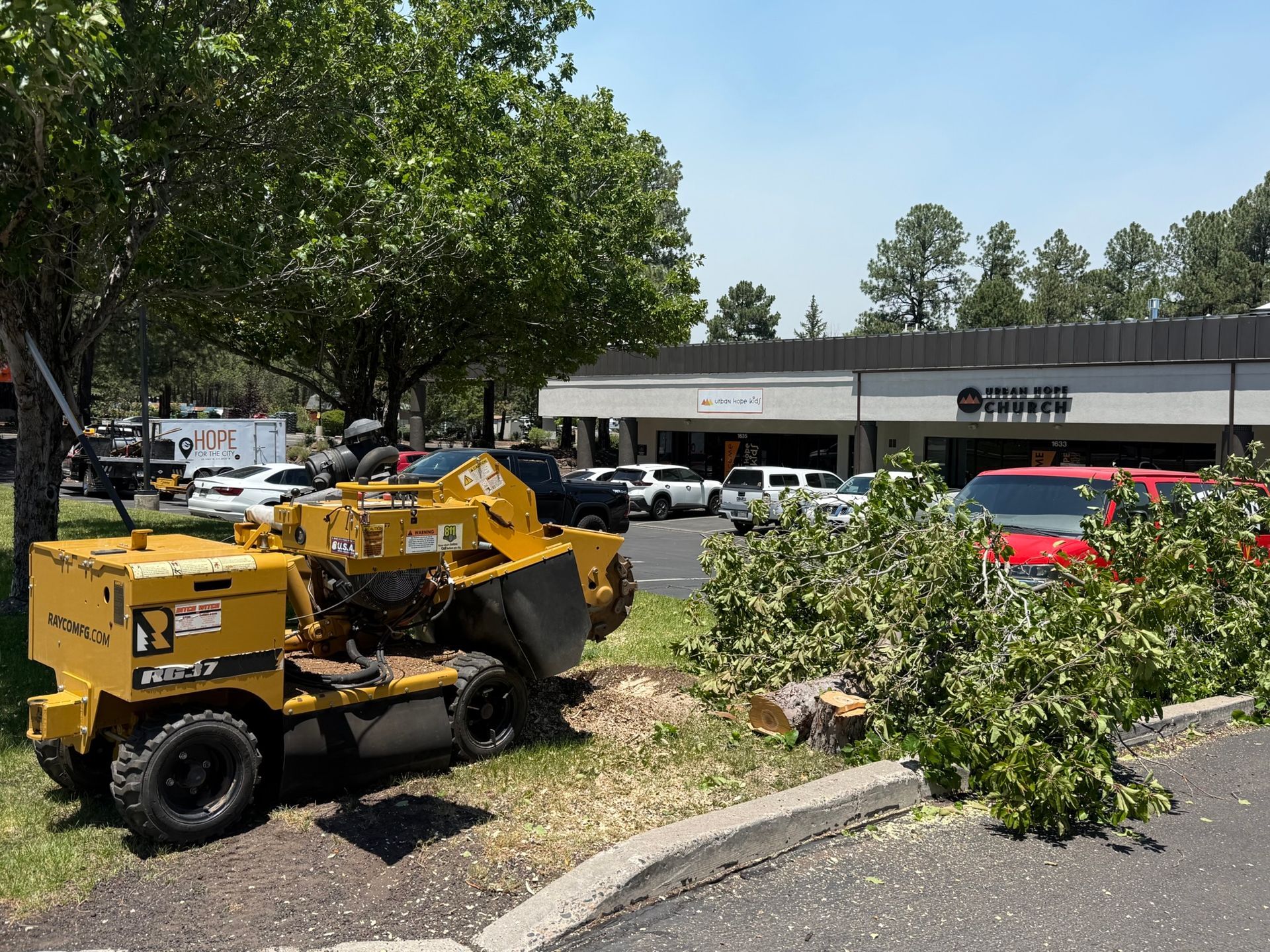 Yellow wood chipper beside downed tree branches in a parking lot near a storefront