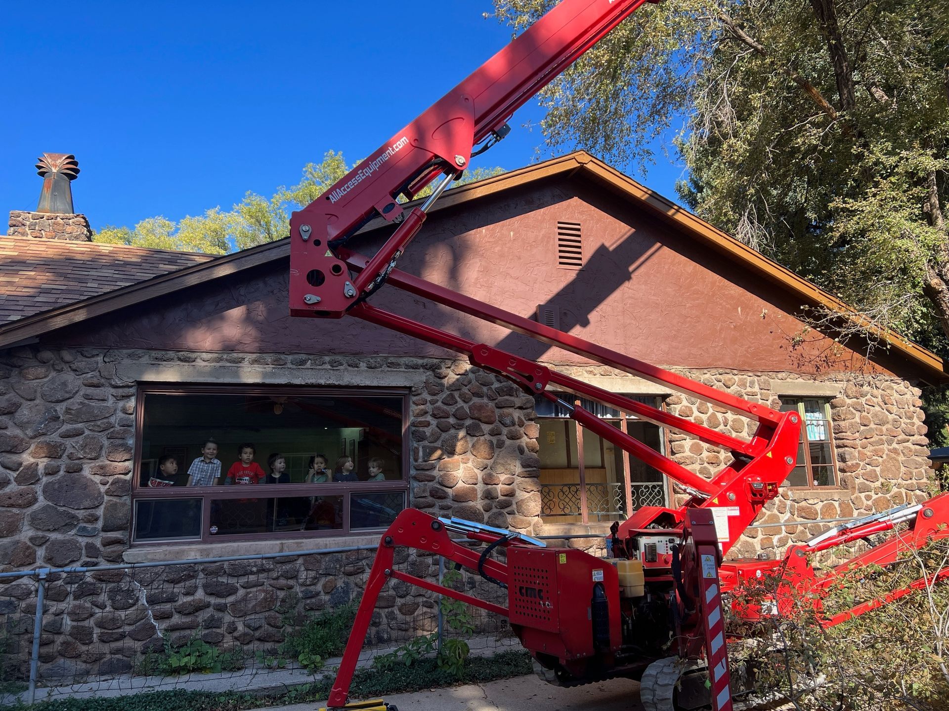 Red cherry picker lifted beside a stone house with people looking out the window