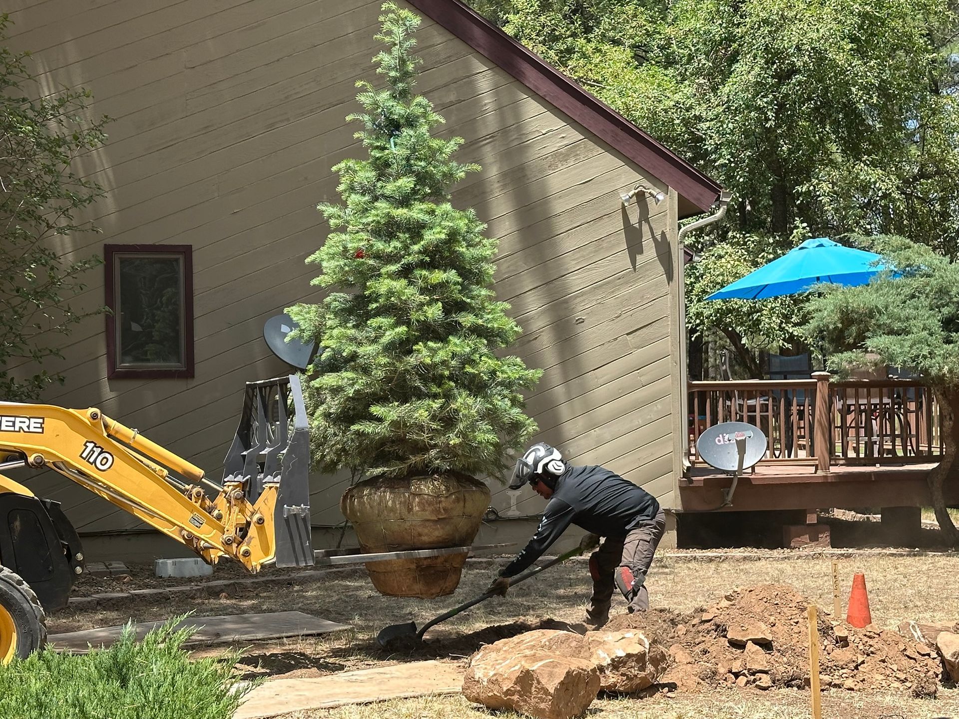 Person digging a trench beside a house with an excavator and wheelbarrow in a backyard