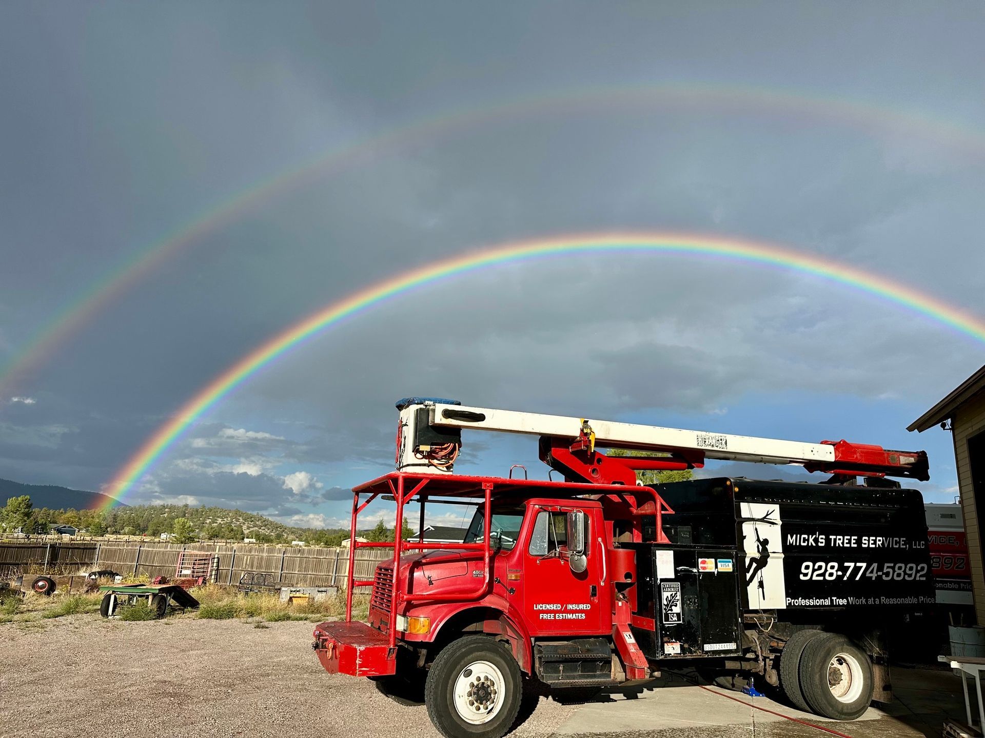 Red utility truck under a double rainbow in a rocky open field