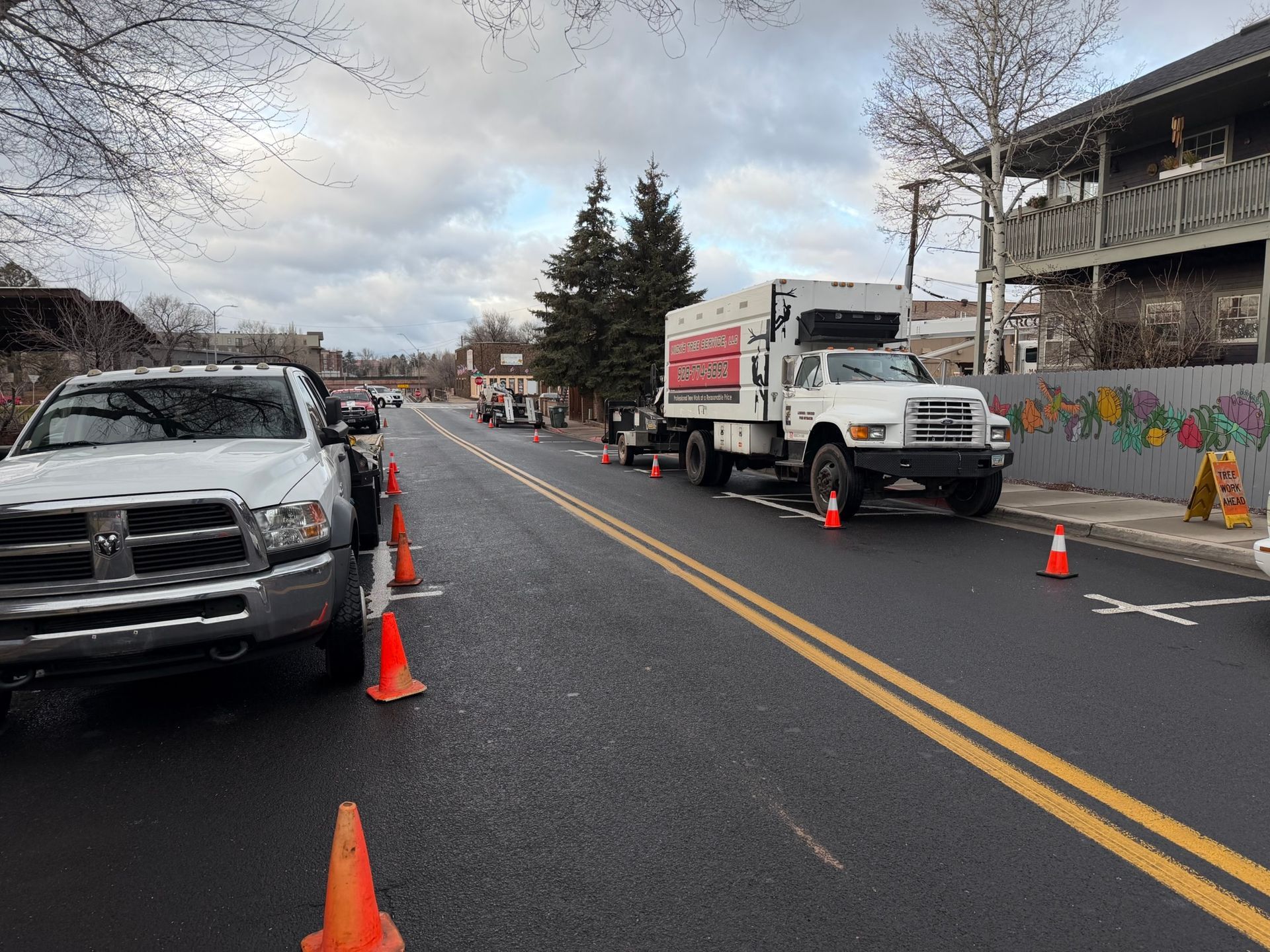 Parked trucks and orange cones blocking a wet street under overcast skies