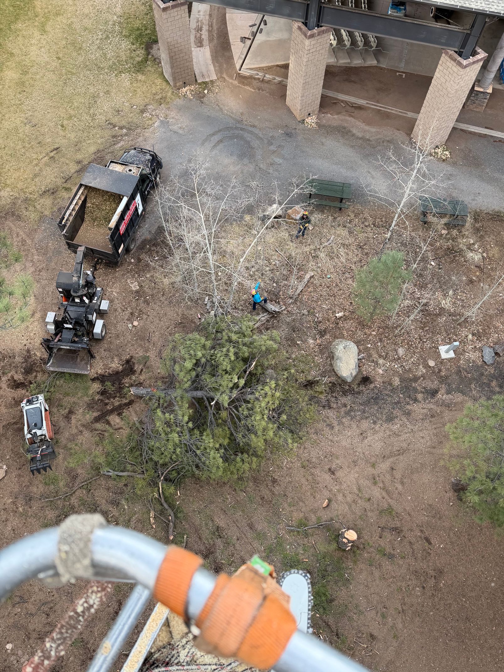 Overhead view of a small excavator at a rubble-strewn construction site beside a building foundation.