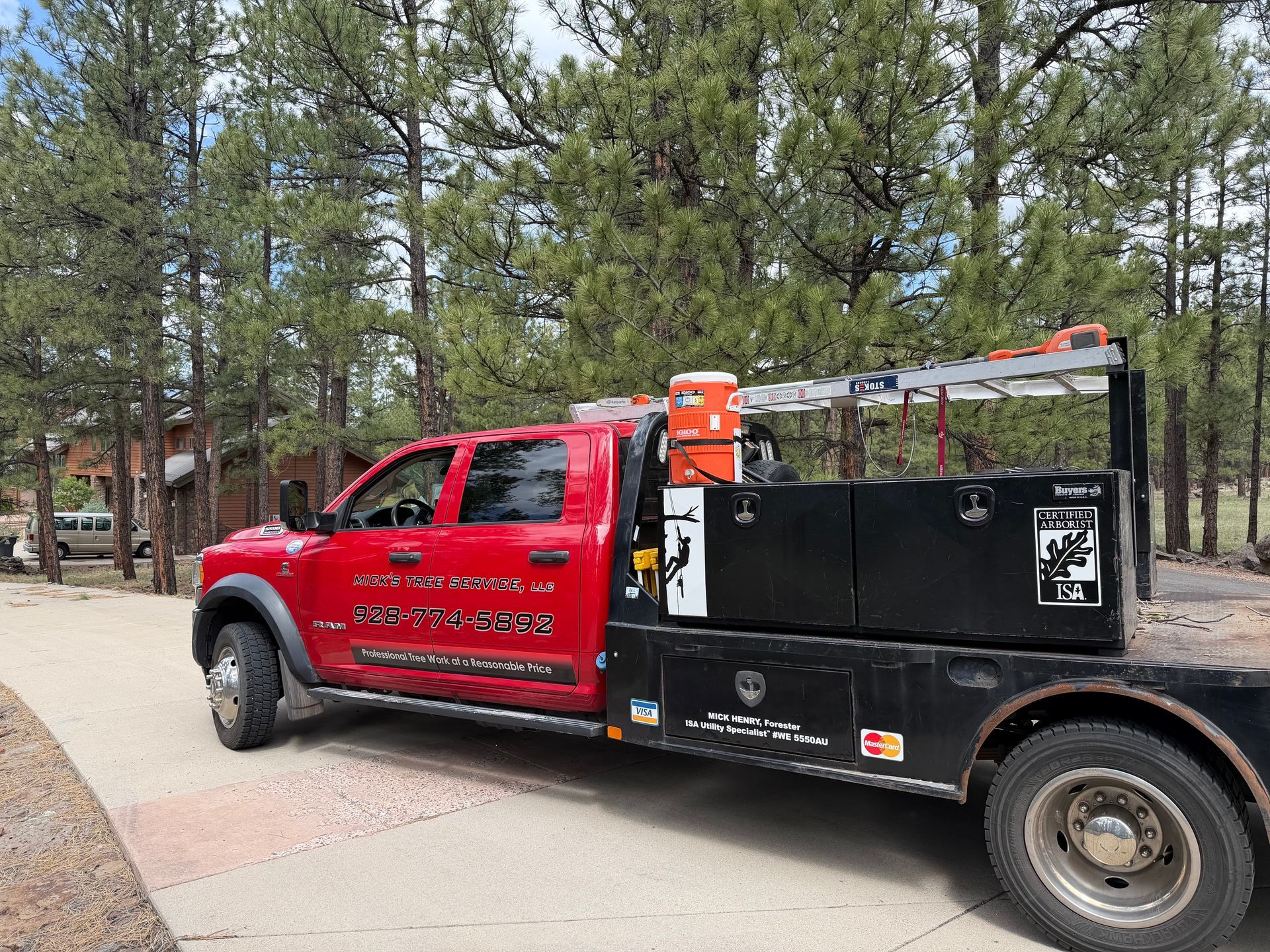 Red utility truck with ladder rack parked beside a wooded walkway