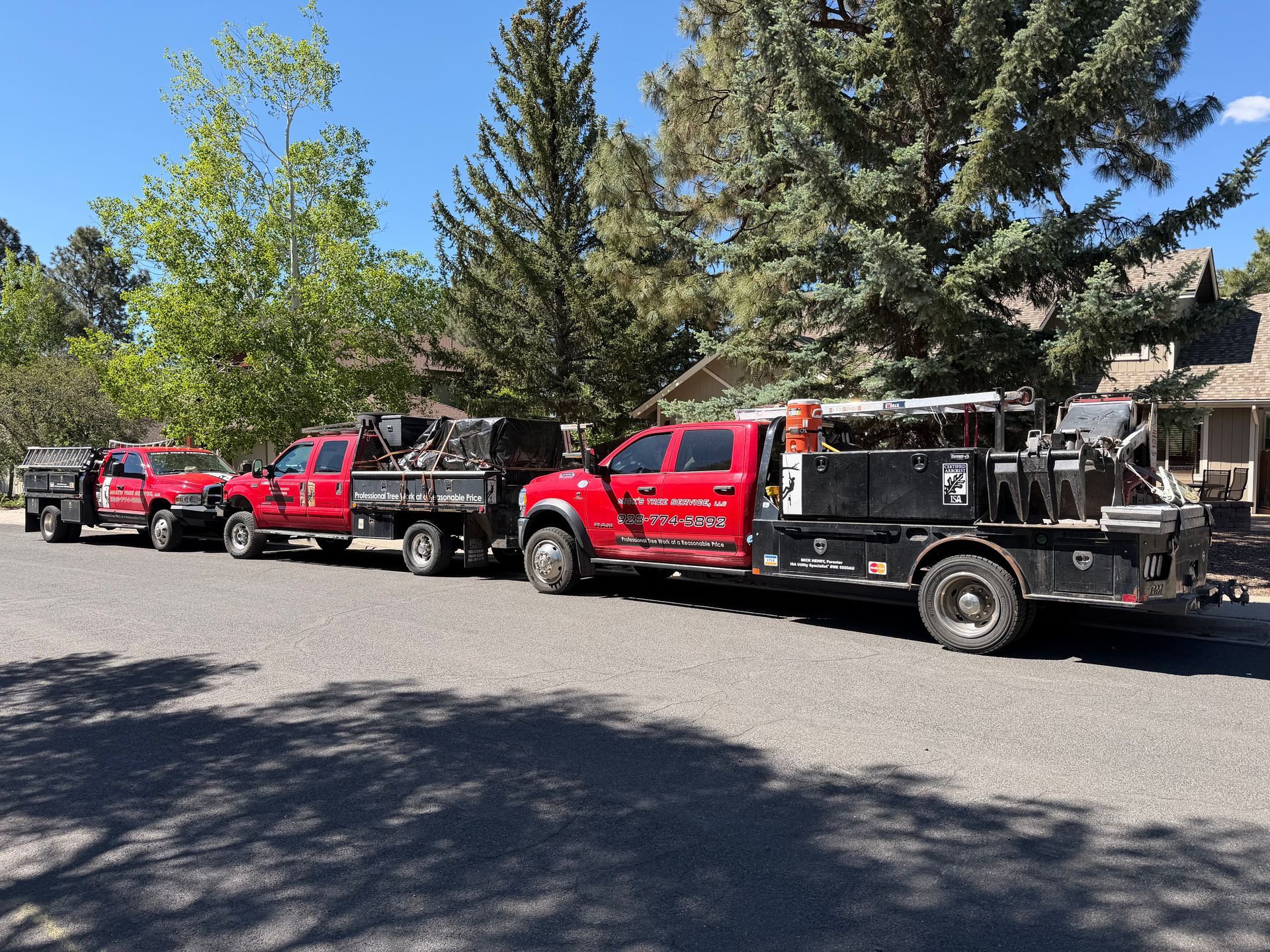 Line of red and black utility trucks parked along a tree-lined street.