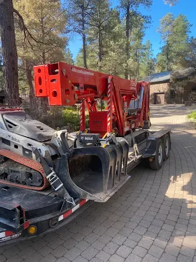 Red heavy machinery mounted on a trailer parked on a stone driveway in a wooded area