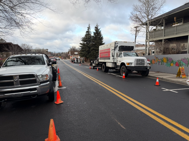 Road closed with parked trucks and orange cones on a city street under cloudy skies