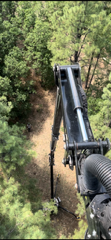 A crane arm extends over a dirt path through dense green trees.