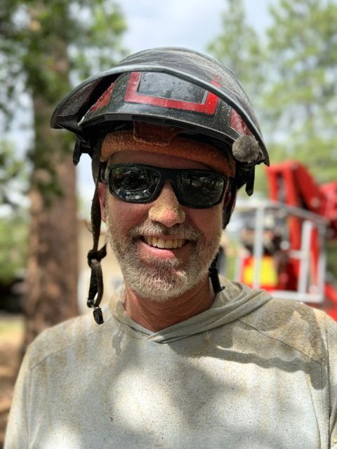 Smiling person wearing sunglasses and a bike helmet outdoors, with a red ladder blurred in the background