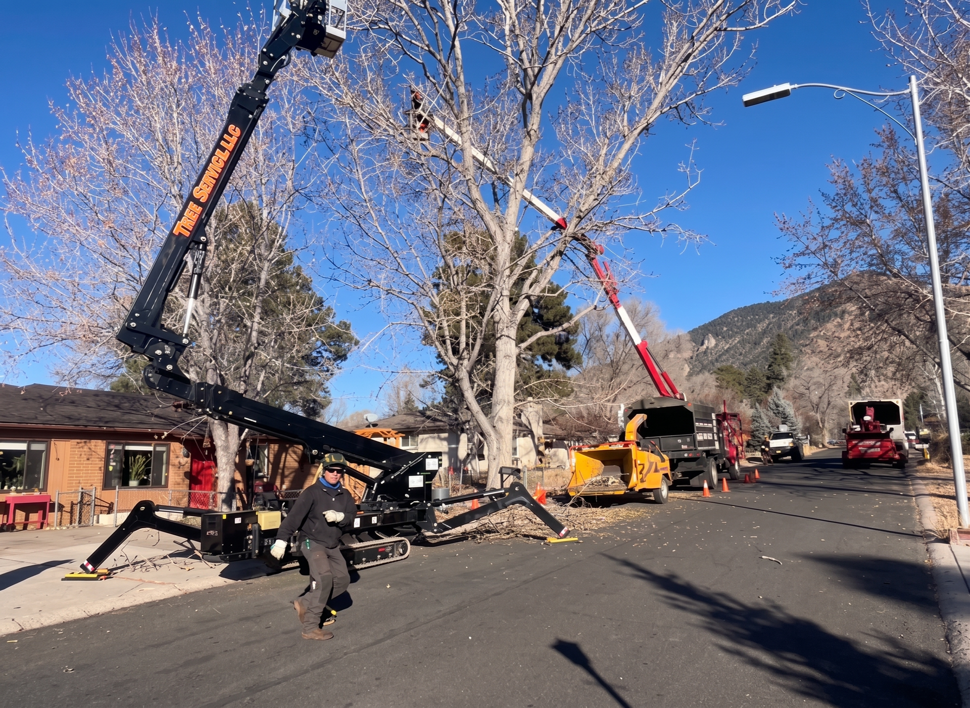 Worker using a chainsaw to cut fallen branches in a yard near a brick wall