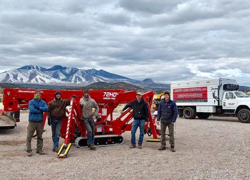 Group of people standing by a red industrial machine and white truck in a snowy mountain landscape