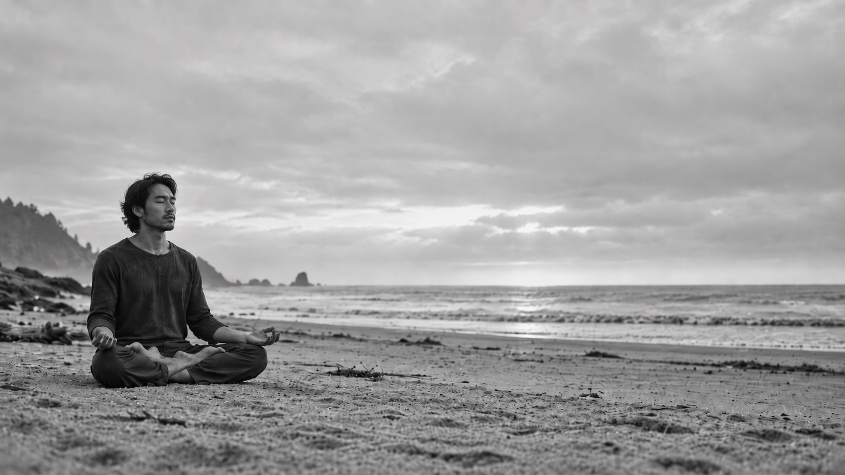 Person meditating on a beach at sunset with waves and cloudy sky in the background