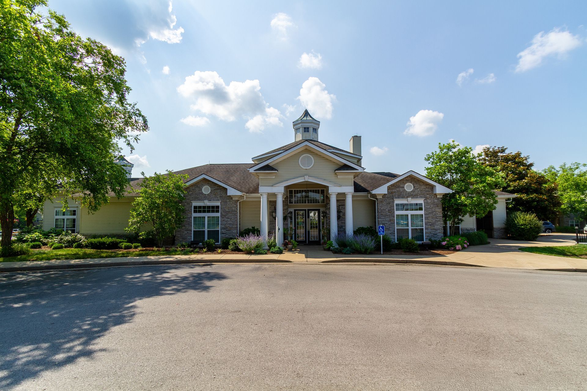 A light-colored resident clubhouse with a peaked roof, stone accents, and columns; sunny day with a blue sky. Come experience comfortable living in our Apts Lexington, KY residents love.