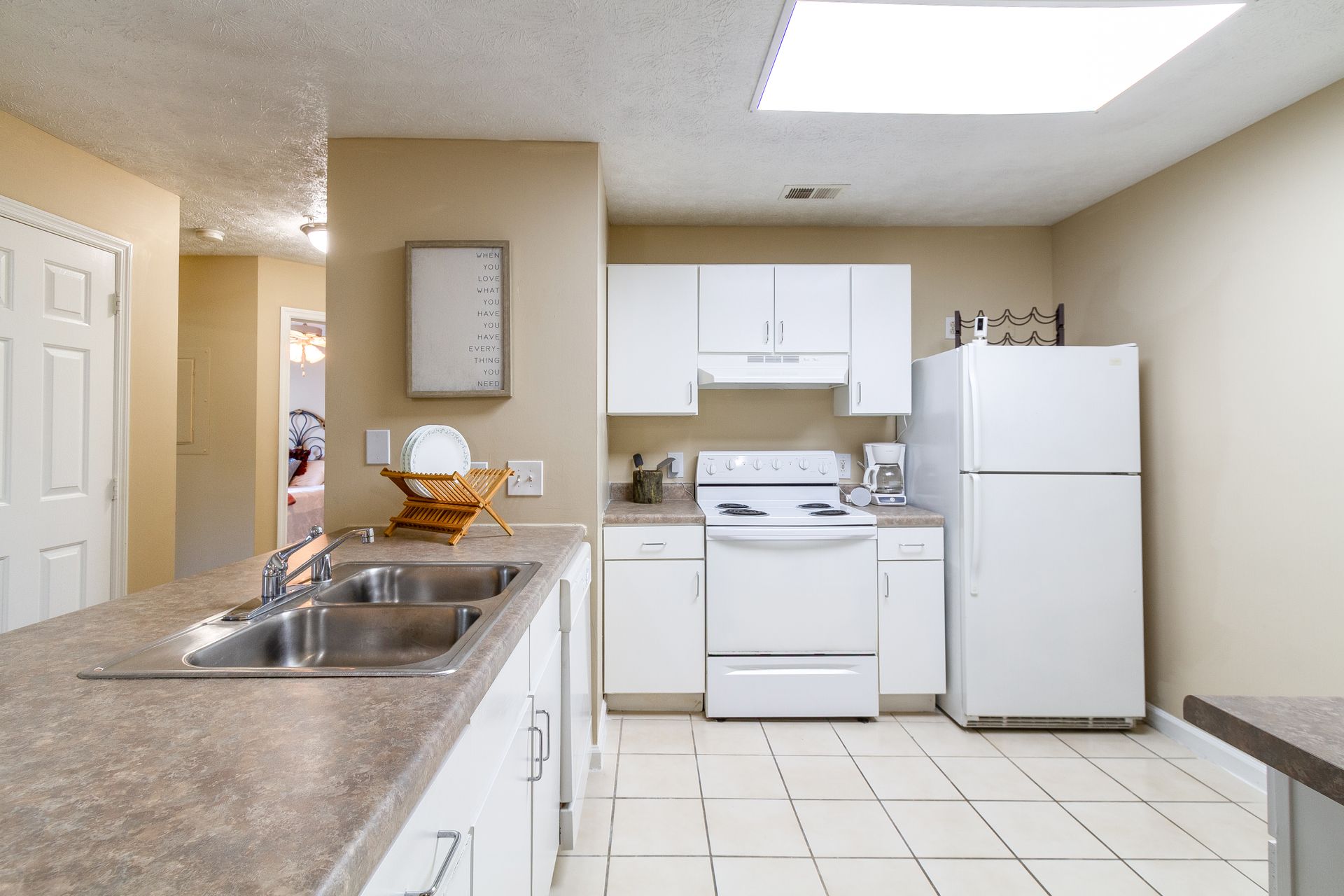 Kitchen with white cabinets, appliances, and tile floor, a countertop with sink, and a door to a hallway. Step inside our spacious 1-bedroom apartments for rent in Lexington, KY today.
