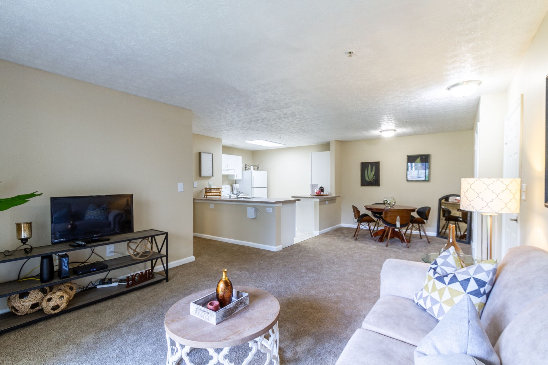 Living room with couch, TV, and dining area. Neutral color scheme, carpet flooring, open layout. See what makes our Lexington, KY apts a comfortable place to call home.