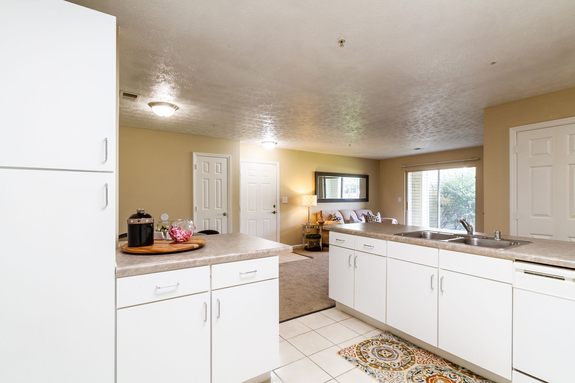 White kitchen with countertops and cabinets, leading to a living room with couch and sliding door. Tour our expansive 3-bedroom apartments for rent in Lexington, KY and find your fit.